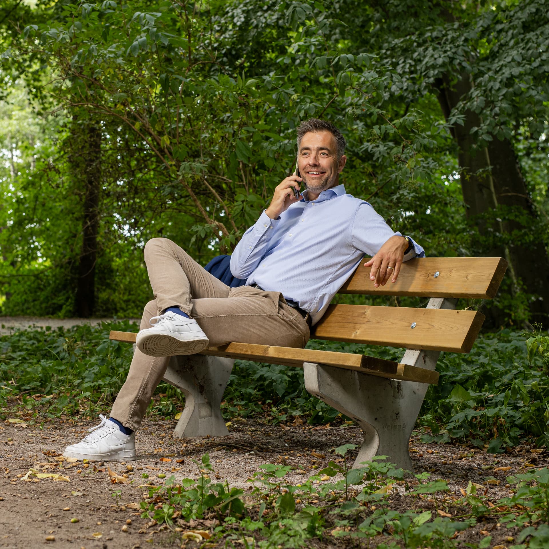 Siemon van Dam in gesprek aan de telefoon op een bankje in het park
